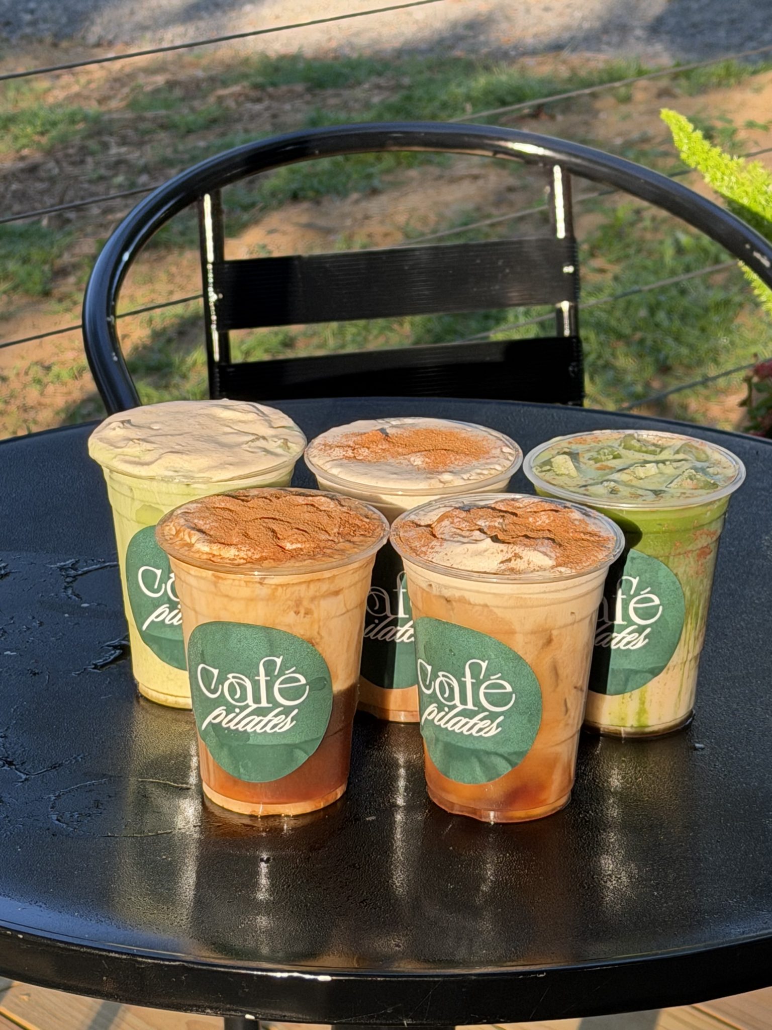 Four iced drinks in Cafe Pilates cups on an outdoor table