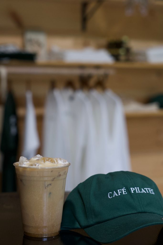 An iced coffee beside an embroidered Cafe Pilates cap